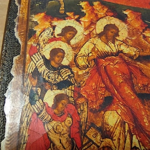 May include: Close-up of a religious icon depicting figures in robes with halos, set against a backdrop of warm orange and yellow hues. The icon has a distressed, aged appearance, with visible cracks in the paint. The frame is dark brown with a textured edge.