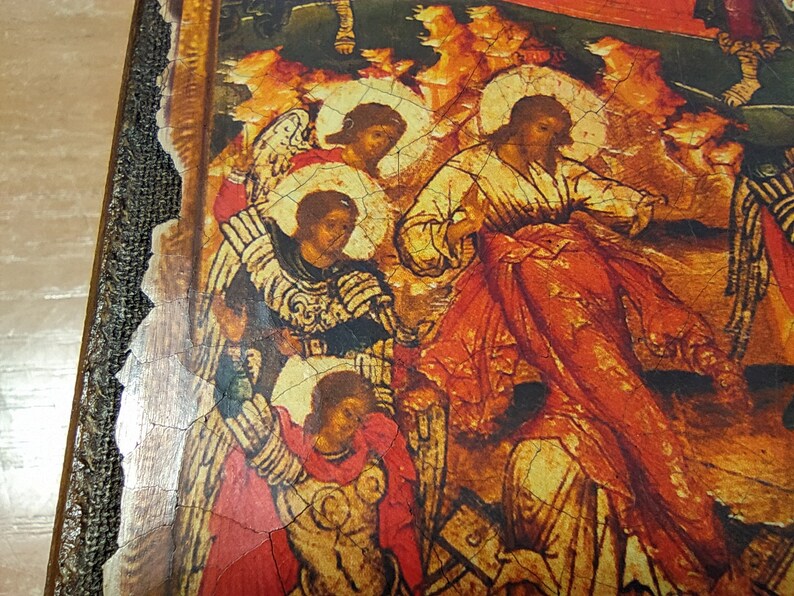 May include: Close-up of a religious icon depicting figures in robes with halos, set against a backdrop of warm orange and yellow hues. The icon has a distressed, aged appearance, with visible cracks in the paint. The frame is dark brown with a textured edge.