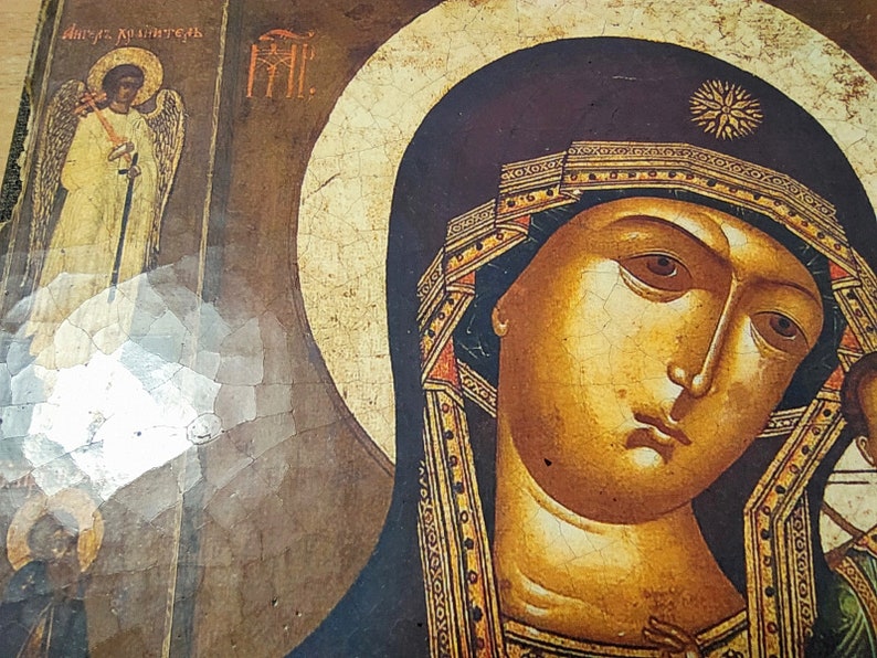 Puede incluir: Un icono vintage que representa a la Virgen Mar&iacute;a sosteniendo a un beb&eacute; Jes&uacute;s. El icono est&aacute; pintado en un panel de madera y tiene un aspecto agrietado y envejecido. La Virgen Mar&iacute;a lleva una t&uacute;nica azul oscuro con ribetes dorados y una corona. El beb&eacute; Jes&uacute;s lleva una t&uacute;nica blanca. El icono est&aacute; enmarcado en un sencillo marco de madera.