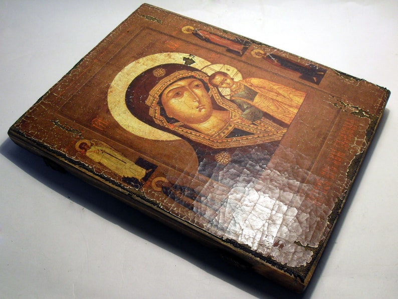 Puede incluir: Un icono de madera vintage que representa a la Virgen Mar&iacute;a y al ni&ntilde;o Jes&uacute;s. El icono est&aacute; pintado en tonos dorados, rojos y azules y tiene un aspecto desgastado y antiguo. El icono est&aacute; enmarcado en un sencillo marco de madera.