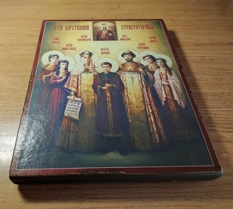 May include: A framed religious icon depicting a family of seven people. The icon is painted in a traditional style with gold accents. The text at the top of the icon reads "Эти царственные" and "Страстотерпцы".