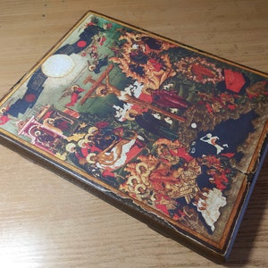 May include: A rectangular, wooden religious icon featuring a detailed, colorful depiction of a biblical scene. The artwork includes figures, crosses, and architectural elements, with a distressed, aged appearance. The icon has a dark brown border.