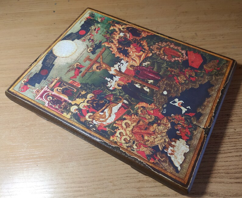 May include: A rectangular, wooden religious icon featuring a detailed, colorful depiction of a biblical scene. The artwork includes figures, crosses, and architectural elements, with a distressed, aged appearance. The icon has a dark brown border.