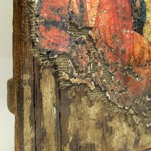 May include: A close-up of a wooden frame with a faded, red and orange painting. The paint is peeling and cracking, revealing the wood underneath. The frame is weathered and has a rustic appearance.
