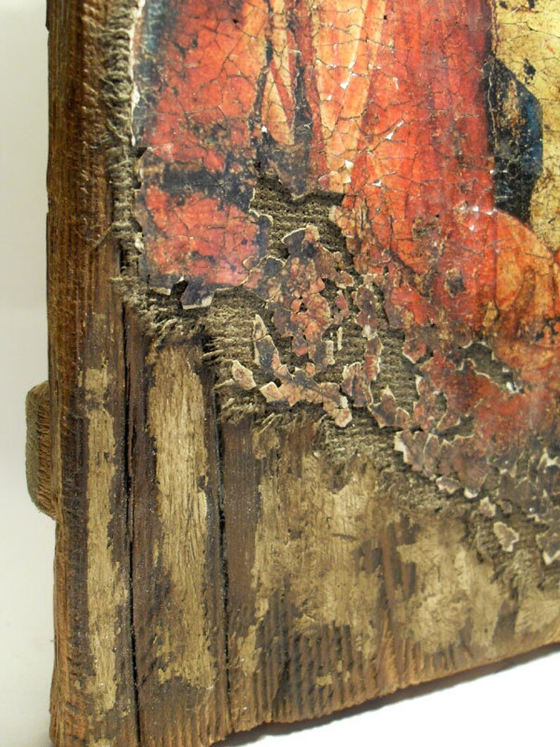 May include: A close-up of a wooden frame with a faded, red and orange painting. The paint is peeling and cracking, revealing the wood underneath. The frame is weathered and has a rustic appearance.