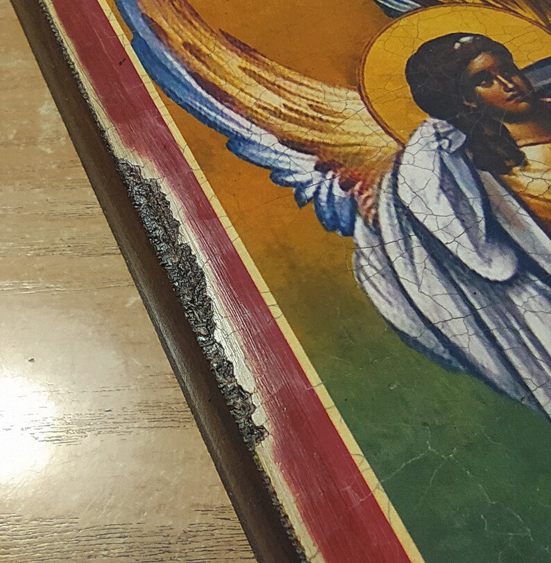 May include: A vintage-style religious icon with a painted image of an angel with wings. The icon is framed in a dark wood frame with a red and gold border.