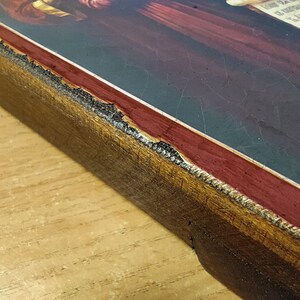 May include: Close-up of the edge of a wooden frame with a red and gold border. The frame is slightly damaged, with some of the gold paint chipped away.