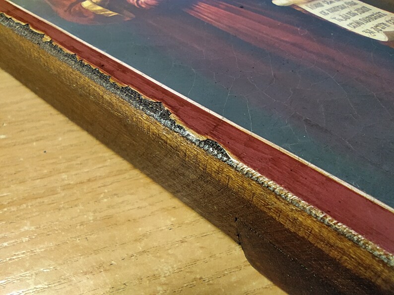 May include: Close-up of the edge of a wooden frame with a red and gold border. The frame is slightly damaged, with some of the gold paint chipped away.