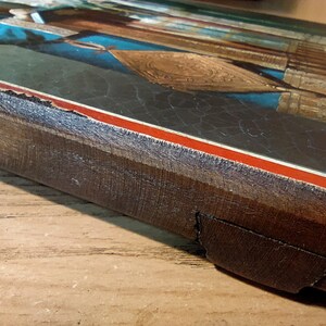 Puede incluir: Un marco de madera con un borde rojo y blanco rodea un icono religioso vintage. El marco tiene un aspecto desgastado y deteriorado, con parte de la madera faltante.