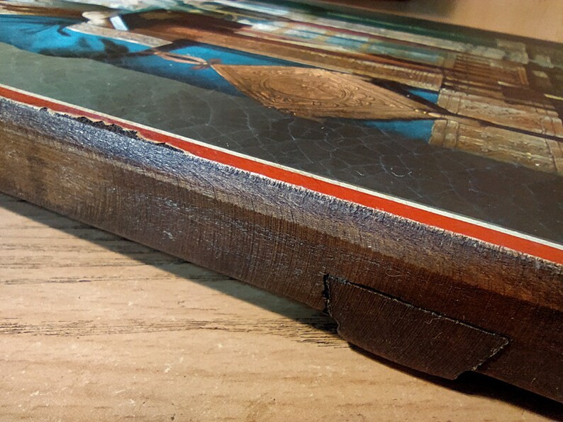 Puede incluir: Un marco de madera con un borde rojo y blanco rodea un icono religioso vintage. El marco tiene un aspecto desgastado y deteriorado, con parte de la madera faltante.