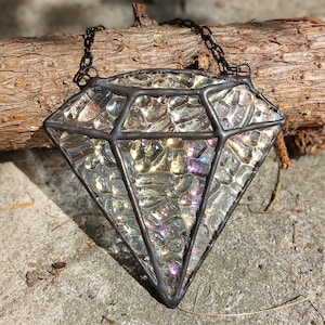 Peut inclure: Une fenêtre en verre coloré en forme de diamant suspendue à une chaîne noire. Le verre est iridescent et a une surface texturée.