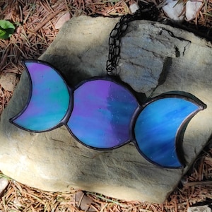 May include: A stained glass triple moon pendant with a black chain. The moon phases are in shades of blue, purple, and green.