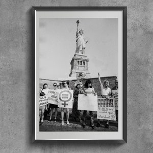 Può includere: Fotografia in bianco e nero di un gruppo di donne che tiene cartelli davanti alla Statua della Libertà. I cartelli recitano "Diritti uguali per le donne", "Grandi donne, grandi problemi", "Tutti gli uomini sono creati uguali, e noi?" e "Diritti uguali per le donne".
