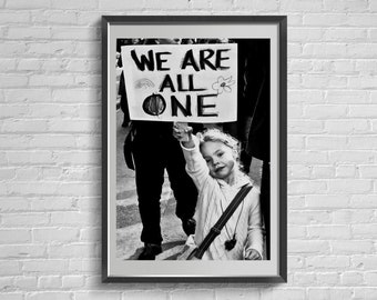 Può includere: Una fotografia in bianco e nero di una bambina che tiene un cartello con su scritto "We are all one". Il cartello ha un arcobaleno e un fiore disegnati. La bambina sorride e guarda la fotocamera.