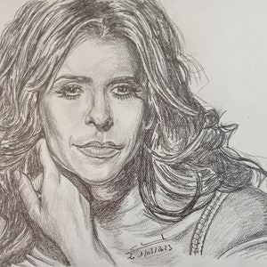 Puede incluir: Un dibujo a lápiz en blanco y negro de una mujer con el pelo largo. Ella está mirando al espectador con una sonrisa suave. Su mano está descansando sobre su mejilla. El dibujo está firmado y fechado "L. 1/03/2023".