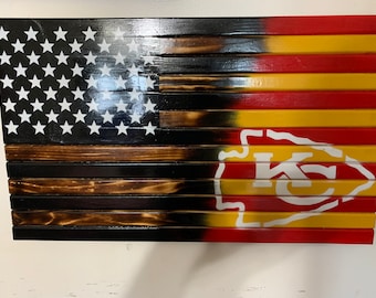 Può includere: Una bandiera americana in legno con una finitura in legno bruciato. La bandiera è divisa a metà, con la metà superiore che è la bandiera americana tradizionale e la metà inferiore che presenta il logo dei Kansas City Chiefs in rosso, giallo e bianco.