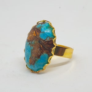 May include: A gold ring featuring a large oval turquoise stone set in a scalloped bezel. The stone has a brown and blue marbled pattern.