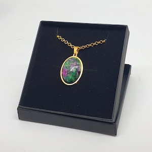 May include: A gold chain necklace with an oval pendant featuring a green and pink gemstone. The necklace is displayed in a black velvet box.