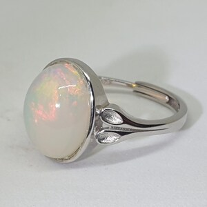 May include: A silver ring featuring a large, oval opal gemstone. The opal has a white base with iridescent flashes of pink and blue.