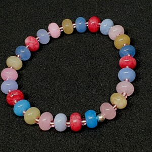 Op de afbeelding: Een kleurrijke kralenarmband met ronde kralen in roze, blauw, geel en rood. De kralen zijn geregen op een dun, elastisch koord. Deze armband is een levendig accessoire. De kralen hebben een diameter van ongeveer 0,8 cm. Perfect om een vleugje kleur toe te voegen.