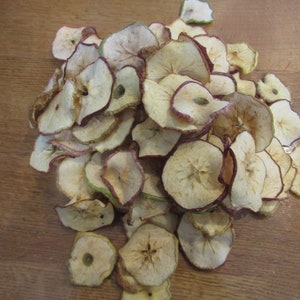 May include: A pile of dried apple slices, some are light brown and some are a darker brown with a reddish hue.