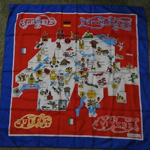 Puede incluir: Un mapa de tela rojo, blanco y azul de Suiza con el nombre del país en cuatro idiomas: "Schweiz", "Switzerland", "Suisse" y "Svizzera". El mapa está lleno de pequeñas ilustraciones de monumentos y símbolos suizos.