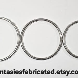 May include: Three silver metal rings of varying sizes are arranged horizontally against a white background. The rings are circular and have a smooth, reflective surface. The Etsy shop URL is visible at the bottom.
