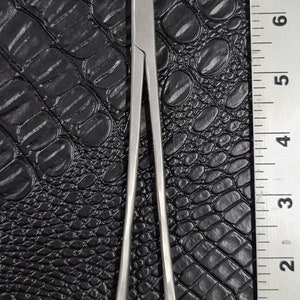 May include: A pair of stainless steel hemostats with a straight jaw design. The hemostats are approximately 6 inches long.