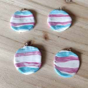 Könnte beinhalten: Vier ovale Ton-Anhänger mit einem Transgender-Pride-Flaggen-Design. Die Anhänger sind in Blautönen, Rosa und Weiß bemalt.