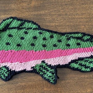 Puede incluir: Un pez de ganchillo verde y rosa con detalles negros. El pez tiene una franja rosa a lo largo de su lado y manchas negras en su espalda.