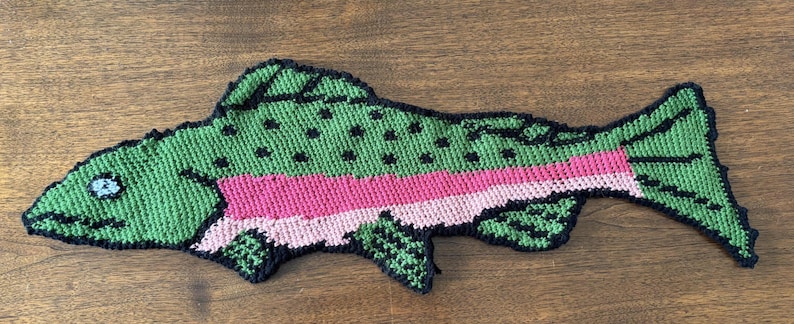 Puede incluir: Un pez de ganchillo verde y rosa con detalles negros. El pez tiene una franja rosa a lo largo de su lado y manchas negras en su espalda.