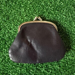May include: A dark brown leather coin purse featuring a smooth, soft texture and a gold-toned metal kiss-lock clasp closure at the top. The small pouch has a rounded, trapezoidal shape with visible natural grain and subtle creases on the surface.