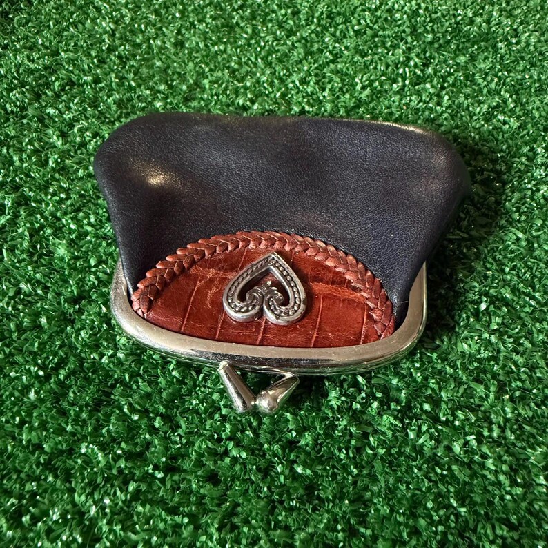May include: A dark navy blue leather coin purse featuring a brown crocodile-textured leather accent panel with a braided border. The purse has a silver-toned metal frame with a kiss-lock closure and a central silver-toned heart-shaped emblem.
