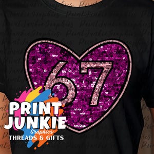 May include: Black t-shirt featuring a sequined heart design with the number 67 in a light pink font. The heart is outlined in a darker pink. The shirt also displays the text "PRINT JUNKIE Graphics THREADS & GIFTS" in a colorful design.