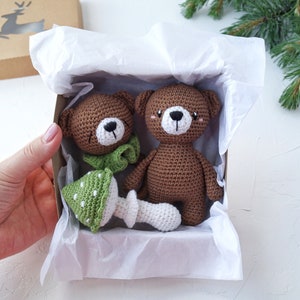 May include: A gift box filled with white tissue paper contains two brown crocheted teddy bears and a green and white crocheted mushroom.