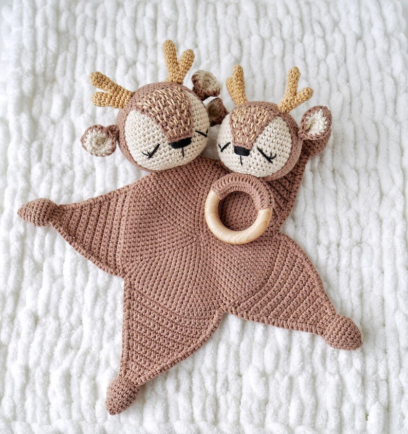 Peut inclure: Une couverture de s&eacute;curit&eacute; pour b&eacute;b&eacute; faite &agrave; la main au crochet, avec deux t&ecirc;tes de cerf aux yeux ferm&eacute;s, des bois beiges et un anneau en bois. La couverture est en forme d'&eacute;toile de couleur rose clair, id&eacute;ale pour un b&eacute;b&eacute;.