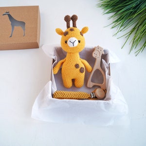 May include: A yellow crocheted giraffe toy with brown spots, a wooden giraffe teether, and a yellow crocheted teething necklace with a wooden clip in a white gift box.