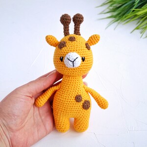 May include: A crocheted yellow giraffe toy with brown spots and ears. The giraffe has a white face with black eyes and a small white nose.