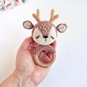 Peut inclure: Un hochet en forme de cerf crochet&eacute;, dans les tons marron, beige et cr&egrave;me. Le cerf a de petits bois, les yeux ferm&eacute;s et une base en anneau de bois. Le hochet est con&ccedil;u pour les b&eacute;b&eacute;s et les jeunes enfants.