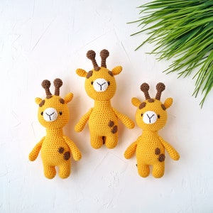 May include: Three crocheted giraffe toys with brown spots and white faces. The giraffes are standing on a white surface.
