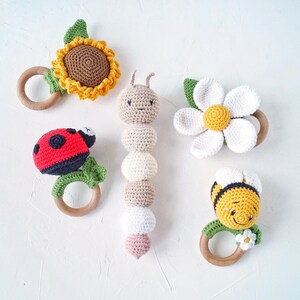 May include: Five crocheted baby teethers with wooden rings. The teethers are shaped like a sunflower, ladybug, caterpillar, daisy, and bee.