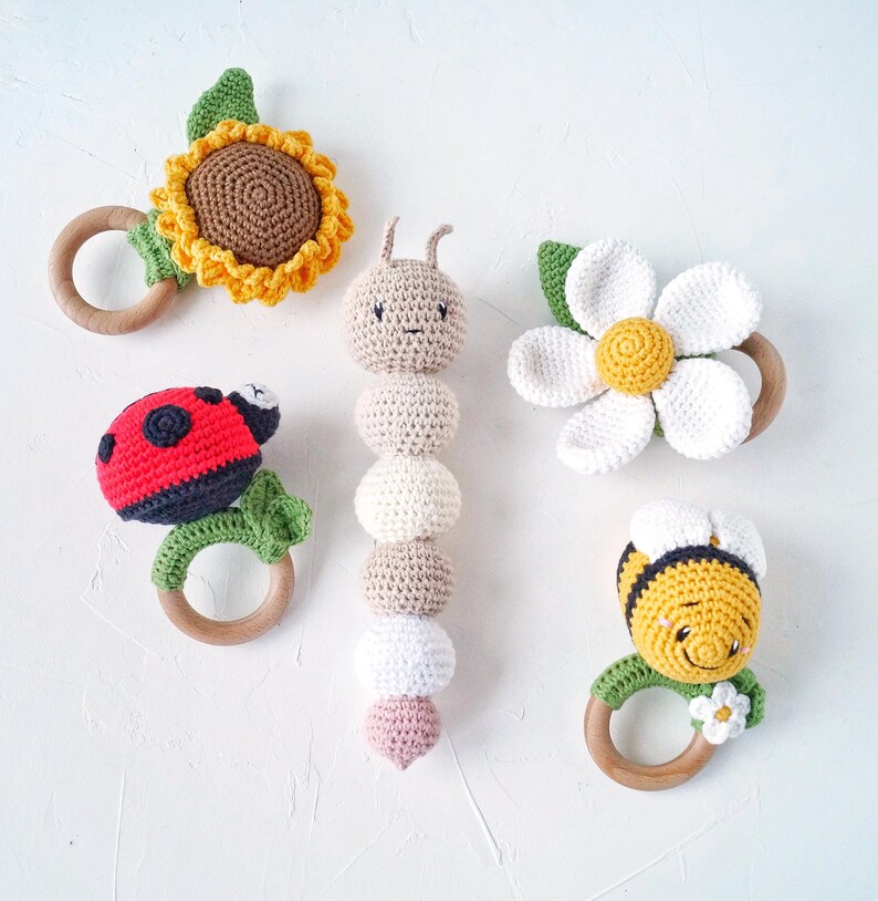 May include: Five crocheted baby teethers with wooden rings. The teethers are shaped like a sunflower, ladybug, caterpillar, daisy, and bee.