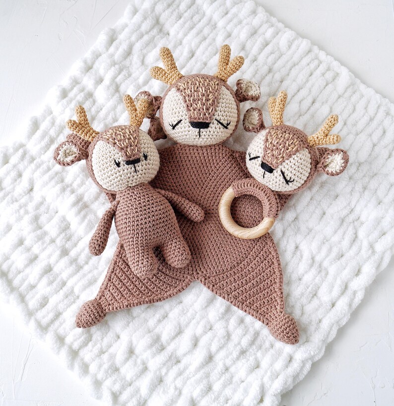 Peut inclure: Ensemble de trois jouets pour b&eacute;b&eacute; sur le th&egrave;me du cerf, crochet&eacute;s. L'ensemble comprend un petit cerf en peluche, une couverture de s&eacute;curit&eacute; en forme de cerf et un hochet en forme de t&ecirc;te de cerf avec un anneau en bois. Les jouets sont dans des tons de marron et beige.