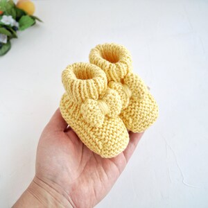 May include: A pair of yellow knitted baby booties with a bow detail. The booties are soft and cosy, perfect for keeping little feet warm.