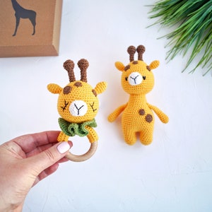 May include: Two crocheted giraffe toys. One giraffe is a rattle with a wooden ring and a green bow. The other giraffe is a plush toy with brown spots.