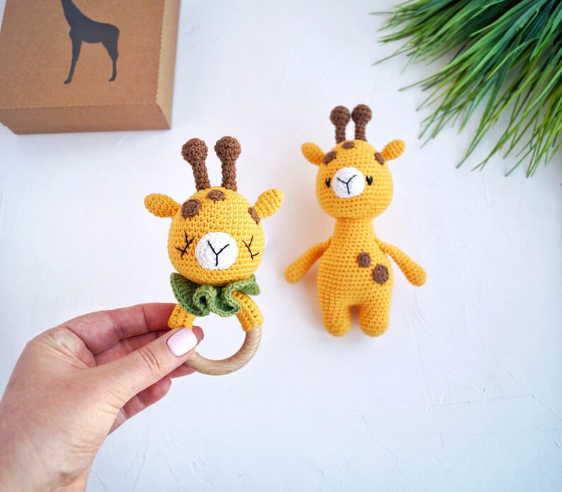 May include: Two crocheted giraffe toys. One giraffe is a rattle with a wooden ring and a green bow. The other giraffe is a plush toy with brown spots.