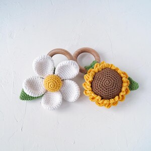 May include: Two crocheted flower teethers, one white daisy and one yellow sunflower, attached to wooden rings.
