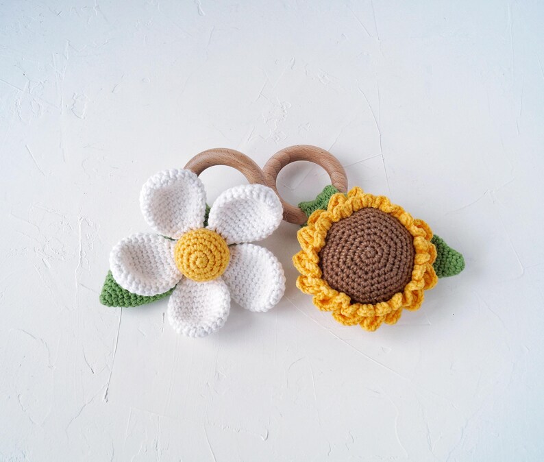 May include: Two crocheted flower teethers, one white daisy and one yellow sunflower, attached to wooden rings.
