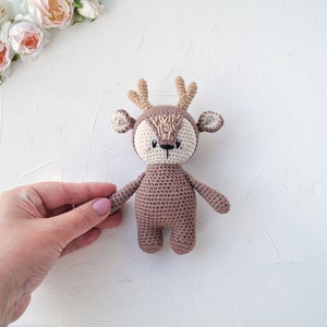 K&ouml;nnte beinhalten: Ein geh&auml;keltes braunes Hirschspielzeug mit wei&szlig;en Akzenten auf dem Gesicht und den Geweih. Der Hirsch sitzt auf einer wei&szlig;en Oberfl&auml;che.