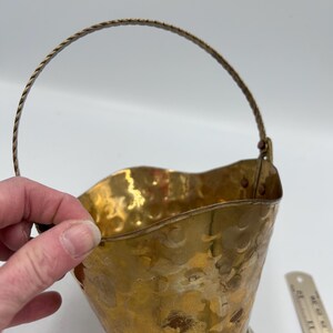 Peut inclure: Un petit seau en laiton martelé avec une poignée en fil torsadé. Le seau a un dessus évasé et une base arrondie. Le laiton a une couleur dorée chaude et une surface texturée. La poignée est fixée avec de petits rivets en laiton.